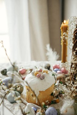 Paskalya yumurtaları, panettone, tavşanlar, kiraz çiçekleri ve nergisler köy masasında. Mutlu Paskalyalar! Modern doğal boyanmış yumurta, şenlikli yemek ve bahar çiçekleri natürmort.