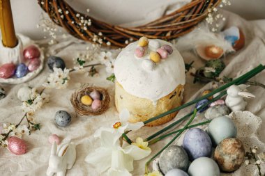 Paskalya yumurtaları, panettone, tavşanlar, kiraz çiçekleri ve nergisler köy masasında. Mutlu Paskalyalar! Modern doğal boyanmış yumurta, şenlikli yemek ve bahar çiçekleri natürmort.