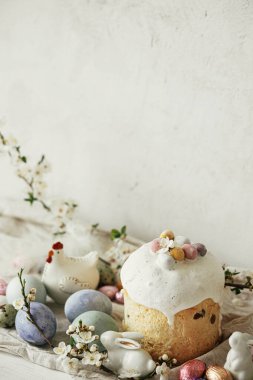 Paskalya yumurtaları, panettone, tavşanlar, kırsal masada kiraz çiçeği kompozisyonu. Mutlu Paskalyalar! Modern doğal boyanmış yumurta, şenlikli yemek ve bahar çiçekleri. Kırsal yaşam