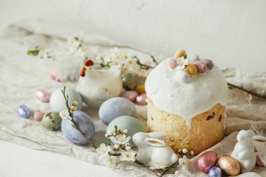 Paskalya yumurtaları, panettone, tavşanlar, kırsal masada kiraz çiçeği kompozisyonu. Mutlu Paskalyalar! Modern doğal boyanmış yumurta, şenlikli yemek ve bahar çiçekleri. Kırsal yaşam