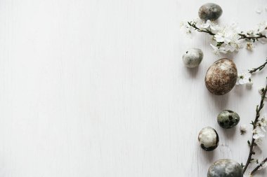 Paskalya düzlüğü. Beyaz kırsal masada paskalya yumurtaları ve kiraz çiçekleri. Mutlu Paskalyalar! Metin için küçük paskalya sınır şablonu. Modern doğal boya mermer yumurta ve bahar çiçekleri.