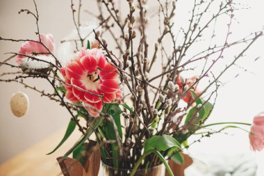 Söğüt dalları, paskalya yumurtaları ve ahşap masa üzerindeki tüyleri olan şık laleler. Mutlu Paskalyalar! Çiftlik evinde basit bir paskalya süsü.