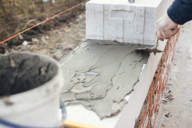 İnşaatçı beyaz blokları kapatıyor. Otoklavla havalandırılmış beton bloklar döşeyen işçiler yapışkan ve malayla çalışıyorlar. İnşaat alanındaki ev inşaatı