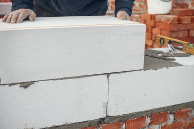 İnşaatçı beyaz blokları kapatıyor. Otoklavla havalandırılmış beton bloklar döşeyen bir işçi. İnşaat alanındaki ev inşaatı