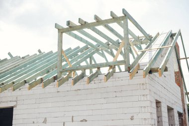 Bitmemiş modern çiftlik evi binası. Mansard ahşap çatı iskeleti, yatakhane ve havalandırmalı beton blok duvarlar. Ağaç kirişleri, kirişler ve kirişler. Yeni ev inşaatı