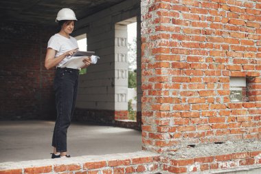 Tabletli şık bir kadın mimar inşaat alanının planlarını kontrol ediyor. Genç bayan mühendis ya da inşaat işçisi yeni modern ev planlarına bakıyor.