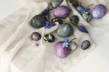 Şık paskalya yumurtaları, yumuşak bahar çiçekleri ve kırsal beyaz masa üzerinde keten kumaş. Mesaj için yer var. Mutlu Paskalyalar! Doğal boyalı mermer ve mor yumurtalar. Mevsimler selamlar