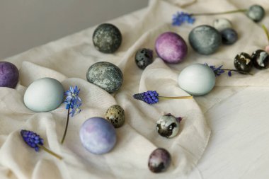 Şık paskalya yumurtaları, yumuşak bahar çiçekleri ve beyaz masa üzerindeki keten kumaş. Bayram afişi. Mutlu Paskalyalar! Doğal boyanmış mermer ve mor yumurtalar.