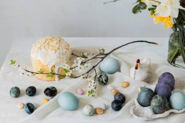 Mutlu Paskalyalar! Paskalya yumurtaları, ev yapımı paskalya ekmeği ve çarşaf peçetesinin üzerindeki bahar çiçekleri duvardaki kırsal masada. Doğal boyanmış mavi ve mermer yumurtalar ve kiraz çiçekleri durgun hayat verir.