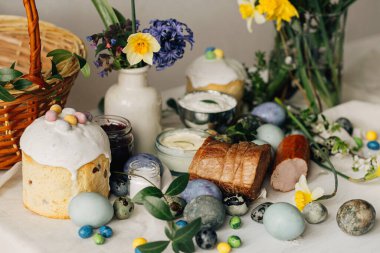 Paskalya yumurtaları, ekmek ve sepet ve kır masasında bahar çiçekleri. Mutlu Paskalyalar! Geleneksel Paskalya bayramı yemeği. Modern doğal boya yumurtaları, lezzetli jambon, ekmek, tereyağı, pancar.