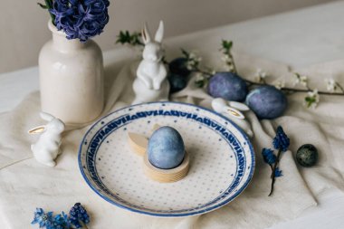 Paskalya sofrası çok şık. Tavşan heykelciğinde paskalya yumurtası, klasik tabakta ve kırsal masada bahar çiçekleri. Mutlu Paskalyalar! Doğal boya mavi yumurta ve mor hiacynt. Tatil için en az yaşam süresi