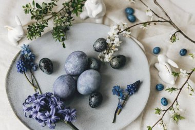 Mutlu Paskalyalar! Klasik tabakta paskalya yumurtaları, tavşan ve keten peçetede bahar çiçekleri, kırsal masa ayarı. Doğal boyalı mavi yumurtalar ve sümbül çiçekleri. Modern durgun yaşam