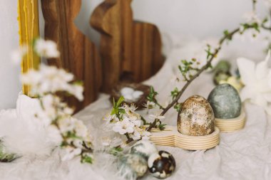 Mutlu Paskalyalar! Şık paskalya yumurtaları, ahşap tavşanlar, kiraz çiçekleri ve kır masasında mum. Modern doğal boyanmış mermer yumurta ve bahar çiçekleri. Paskalya 'da kırsal evdeki hayat dekorasyonu