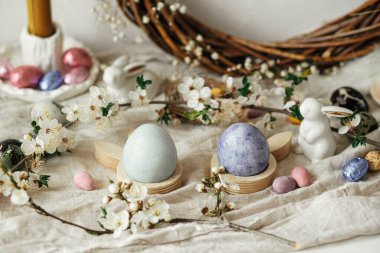 Paskalya yumurtaları, tavşanlar ve kırsal masada kiraz çiçekli kompozisyon. Mutlu Paskalyalar! Modern doğal boyanmış, çikolatalı yumurta ve bahar çiçekleri. Kırsal yaşam