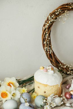 Paskalya yumurtaları, panettone, tavşanlar, kiraz çiçekleri ve nergisler köy masasında. Mutlu Paskalyalar! Modern doğal boyanmış yumurta, şenlikli yemek ve bahar çiçekleri natürmort.