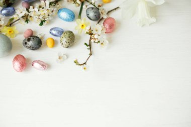 Paskalya düzlüğü. Beyaz kırsal masada paskalya yumurtaları ve kiraz çiçekleri. Mutlu Paskalyalar, mesaj için yer var. Modern doğal boyanmış, çikolatalı yumurta ve bahar çiçekleri. Paskalya bayrağı