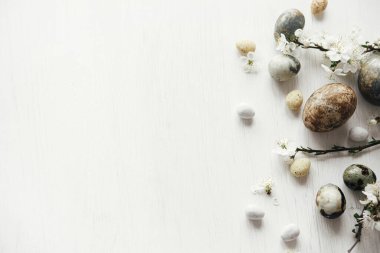 Paskalya düzlüğü. Beyaz kırsal masada paskalya yumurtaları ve kiraz çiçekleri. Mutlu Paskalyalar! Metin için küçük paskalya sınır şablonu. Modern doğal boya mermer yumurta ve bahar çiçekleri.