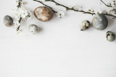 Mutlu Paskalyalar! Paskalya yumurtaları ve kiraz çiçekleri sade beyaz masa yatağında. Modern doğal boya mermer yumurta ve bahar çiçekleri. Metin için en düşük paskalya sınır şablonu