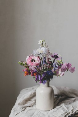 Kırsal keten arka planda şık bir buket. Güzel renkli şakayık, ranunculus, vazoda latilus scabiosa. Yaz çiçekleri, çiçekli karamsar hayat. Metin için boşluk