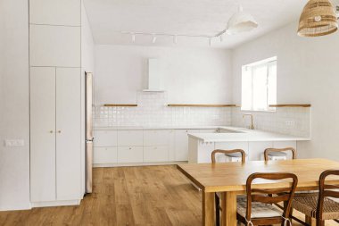 Modern mutfak iç mimarisi. Yeni İskandinav evinde pirinçten düğmeleri, granit tezgahı, aletleri ve ahşap ahşap masası olan şık beyaz mutfak dolapları. Modern mutfak tasarımı.