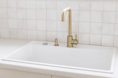 Yeni İskandinav evindeki pencerenin önünde şık bir pirinç musluk ve beyaz granit lavabo var. Modern mutfak iç mimarisi. Modern mutfak tasarımı