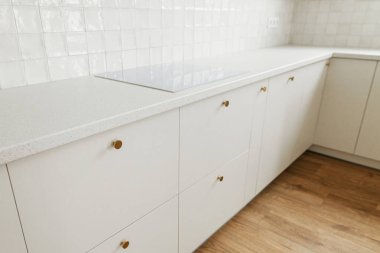 Modern mutfak tasarımı. Yeni İskandinav evinde pirinçten düğmeleri, elektrikli ocağı, beyaz fayansları ve ahşap zemini olan şık beyaz mutfak dolapları. Modern mutfak iç mimarisi.