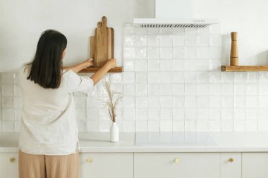 Şık bir kadın rafları çatal bıçakla açıyor ve dekore ediyor. Yeni, minimal beyaz mutfakta tahta kesiyor. Yeni modern İskandinav evine taşındıktan sonra ev hanımı mutfağı temizliyor.