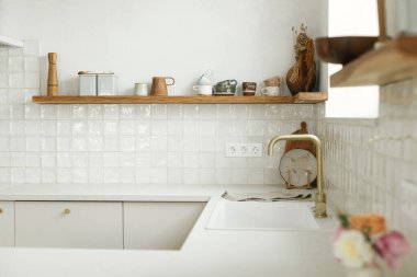 Modern mutfak tasarımı. Pirinç musluğu olan şık beyaz mutfak dolapları, granit tezgah ve yeni İskandinav evinde çatal bıçaklı ahşap raflar. Modern mutfak iç mimarisi