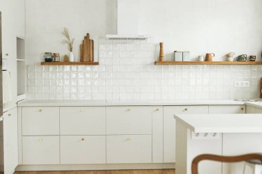 Modern mutfak tasarımı. Pirinç düğmeli şık beyaz mutfak dolapları, granit tezgah, yeni İskandinav evindeki ahşap raflarda aletler ve aletler. Modern mutfak iç mimarisi.