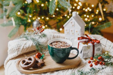 Ilık bir fincan kakao, marşmelov ve çikolatalı kurabiye, noel süsleri ve altın ışıklı şık bir Noel ağacına karşı örülmüş samimi bir arka plan hediyesi. Kış havası
