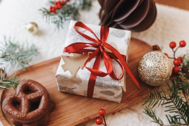 Kırmızı kurdeleli Noel hediyesi, çikolatalı kurabiyeler, Noel süsleri ve ahşap tepsi manzaralı köknar dalları. Mutlu noeller. Xmas arkaplanı