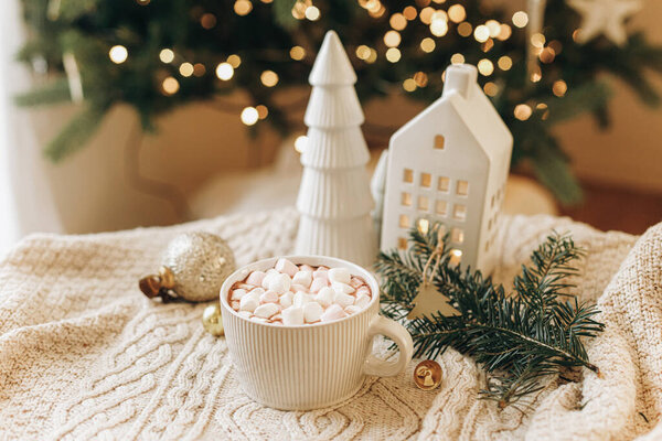 Теплый стакан какао с зефиром, рождественские украшения и елки на уютном трикотажном фоне на стильном рождественском дереве с огнями. Зимнее настроение. Счастливого Рождества!