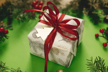 Mutlu Noeller! Kırmızı kurdele, yeşil köknar dalları, kırmızı böğürtlen ve yeşil arka planda altın süslemeleri olan şık bir Noel hediyesi. Xmas geçmişi. Mutlu Noeller.