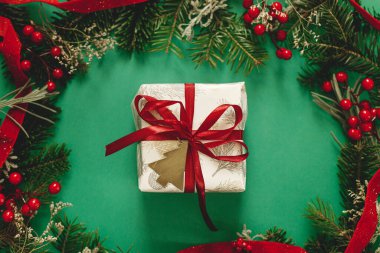 Şık bir Noel hediyesi. Kırmızı kurdele, yeşil köknar dalları, kırmızı böğürtlen ve yeşil arka planda altın süslemelerle modern Noel hediyesi. Xmas geçmişi. Sezonun tebrik kartı.