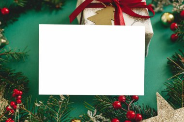 Boş tebrik kartı ve köknar dalları, kırmızı böğürtlen, yeşil arka planda hediye kutusu. Mesaj atmak için yeri olan bir Noel kartı modeli. Xmas kartpostalı. Mevsim tebrik kartı şablonu