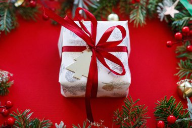 Güzel bir Noel hediyesi. Kırmızı kurdele ve yeşil köknar dallarıyla modern Noel hediyesi, kırmızı arka planda kırmızı böğürtlen. Xmas geçmişi. Sezonun tebrik kartı.