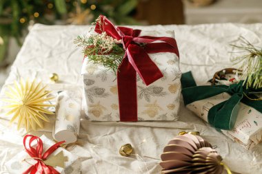 Mutlu Noeller ve mutlu tatiller. Kırmızı ve yeşil kurdeleli şık Noel hediyeleri, köknar dalları, eski oyuncaklar ve kırsal masadaki modern süsler. Paketlenmiş Noel hediyeleri, bayram afişleri