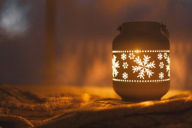 Mutlu Noeller! Şık, ışıl ışıl bir Noel feneri ve akşam karlı bir pencerede rahat bir süveterin üzerinde altın ışıklar. Atmosferik büyülü sahne. Noel tatili afişi. Metin için boşluk