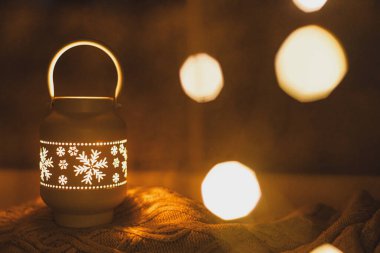 Mutlu Noeller! Pırıl pırıl parlayan Noel feneri ve altın ışıklar karlı pencerenin önünde, rahat bir süvetere takılıyor. Atmosferik büyülü sahne. Noel tatili afişi. Metin için boşluk
