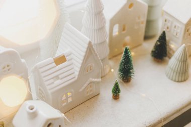 Noel seramik evleri, beyaz karlı ağaçlar ve penceredeki altın ışıklar. Xmas geçmişi. Mutlu Noeller! Atmosferik Noel sahnesi, minyatür tatil köyü