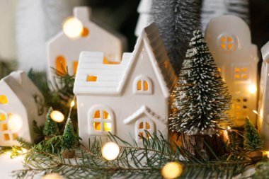 Noel arifesinde küçük seramik evler, karlı ağaçlar ve arka planda altın ışıklar. Mutlu Noeller! Atmosferik Noel sahnesi, minyatür tatil köyü. Xmas arkaplanı
