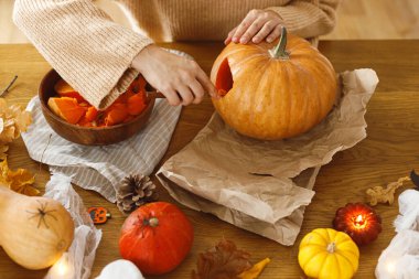 Cadılar Bayramı hazırlığı. Masada balkabağı ve bıçak tutan eller ve oturma odasında hayaletler ve örümcekler. Cadılar bayramı süslemeleri yapmak, mesaj için yer açmak. Bir balkabağı oysana.