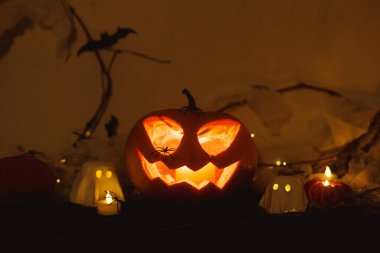 Mutlu Cadılar Bayramı! Ürkütücü Jack o fener kabağı, parlayan hayaletler, karanlıkta örümcekler ve yarasalar. Masada atmosferik cadılar bayramı dekoru var. Şaka mı şeker mi?