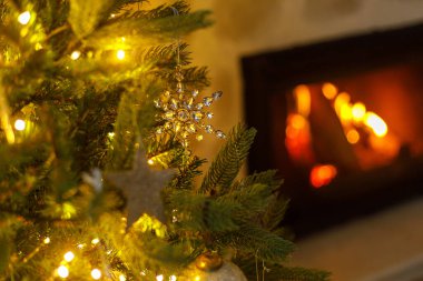 Cam kar tanesi, klasik takılar ve yanan şöminenin arka planında altın ışıklarla süslenmiş güzel bir Noel ağacı. Kış tatili hazırlığı. Atmosfer sihirli arifesi