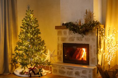 Mutlu Noeller! Şık dekore edilmiş yılbaşı ağacı, eski süsler ve şömine rafının modern dekorasyonuyla akşamları çan, kurdele ve çelenk ışıkları. Evde atmosferik Noel arifesi