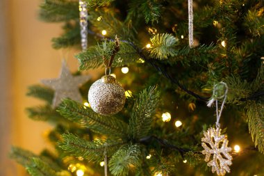 Ağaca asılmış şık bir Noel süsü. Cam kar taneleri, klasik takılar ve altın ışıklarla süslenmiş güzel bir Noel ağacı. Kış tatili hazırlığı. Atmosfer sihirli arifesi