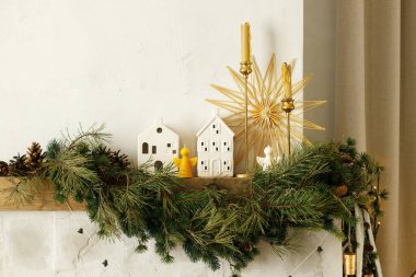 Süslü Noel şöminesi şömine rafı köknar dalı, mumlar, seramik evler, çanlar, kurdele. Modern İskandinav odasında şenlikli Xmas kış dekoru. Mutlu Noeller.!
