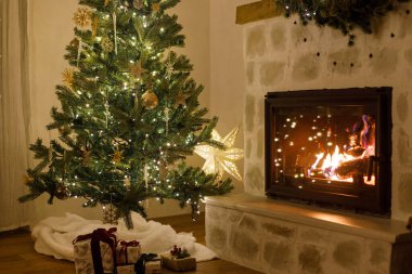 Şık dekore edilmiş yılbaşı ağacı, eski süsler ve şömine rafının modern dekorasyonuyla akşamları çan, kurdele ve çelenk ışıkları. Evde atmosferik Noel arifesi. Mutlu Noeller.!