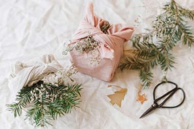 Sıfır Noel konsepti. Renkli Noel hediyeleri, keten kumaşa sarılı, yeşil köknar dalı, kır masasında, doğal süslemelerle. Sürdürülebilir yaşam tarzı, Furoshiki sunar