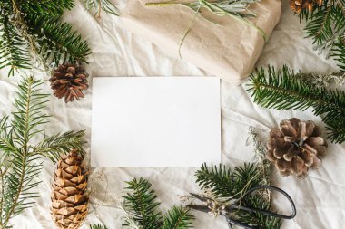 Noel kartı maketi. Boş tebrik kartı ve sade çam kozalakları ve köknar dalları olan köy masasında şık sıfır atık hediye. Mesaj için yer var. Mevsimin tebrik kartı şablonu. Çevre dostu